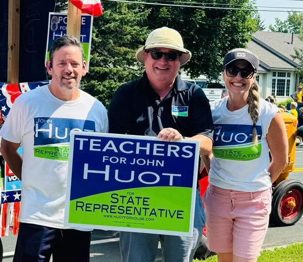 John Huot standing with local educators and parade volunteers holding campaign signs
